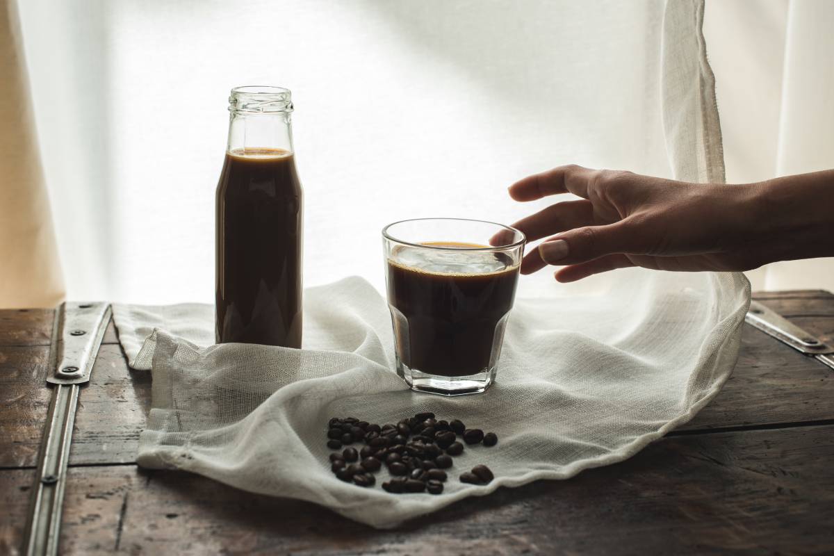 Person taking glass of coffee from cloth with roasted coffee beans