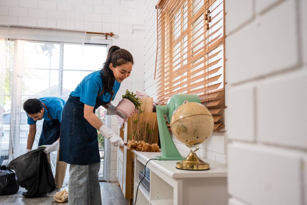 Asian young man and woman cleaning service worker work in living room. Attractive housekeeper cleaner team wear apron and cleaning messy dirty floor for housekeeping housework and chores in house.