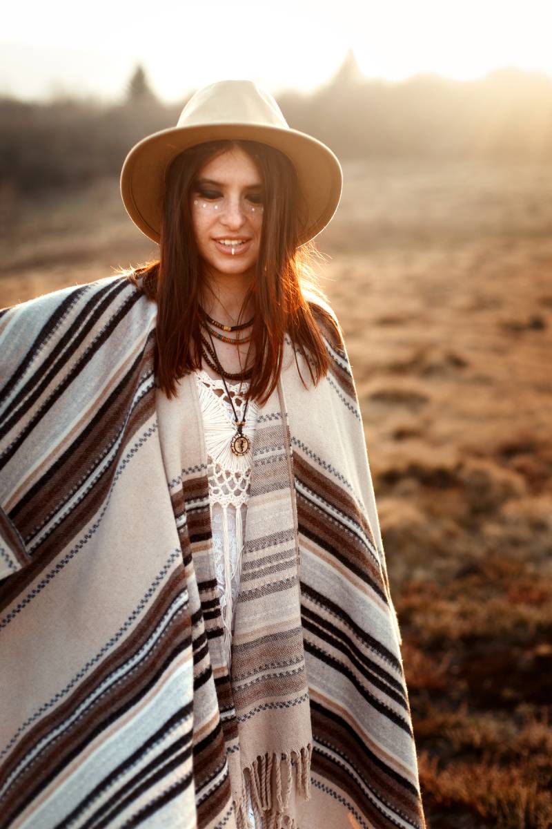 beautiful woman hipster posing, wearing hat and poncho, at sunset in mountains, true emotions, sensual look