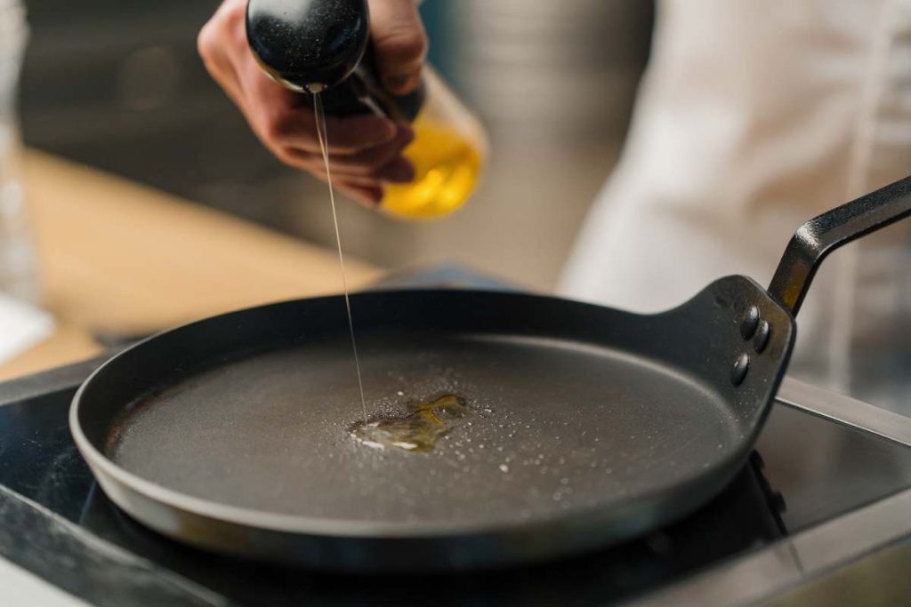 A professional kitchen chef greases frying pan with oil