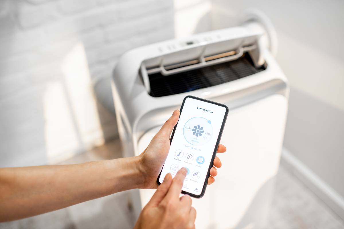 Woman holding smart phone with launched application for air condition control with ventilation unit on the background. Smart home concept