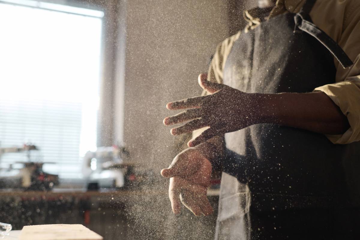 Black Carpenter Brushing Sawdust Off of Hands with Cloud in Air