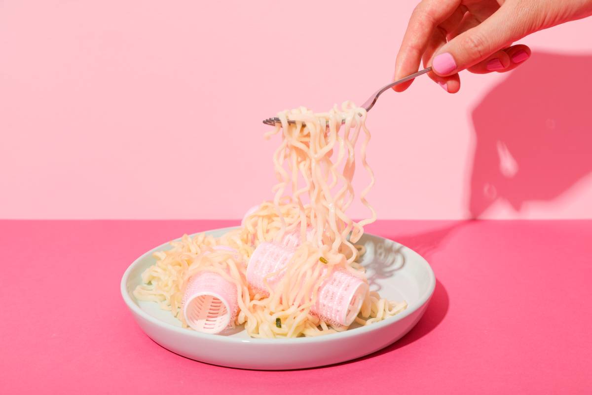 Noodles and curlers in plate, female hand on pink background