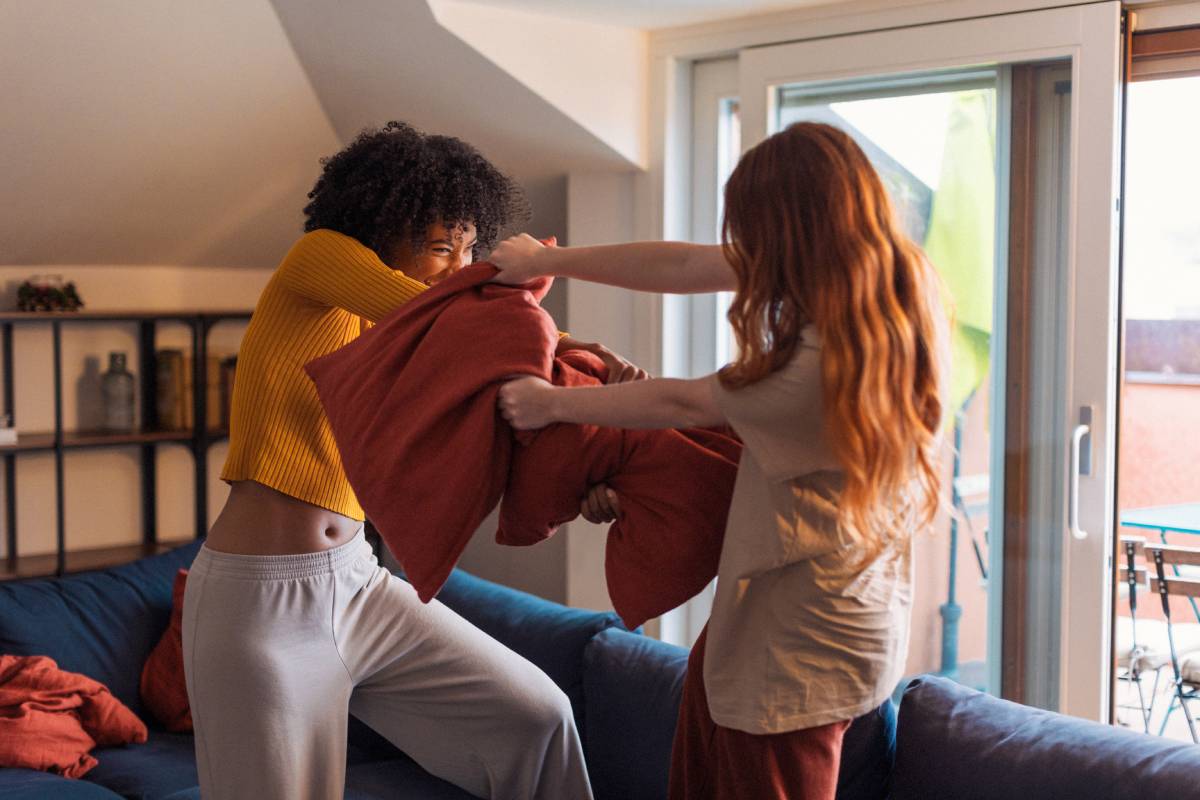 Two joyful female friends are having a pillow fight in the living room